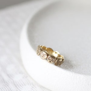 May include: A gold ring with a band of small, detailed skull charms. Each skull has a small diamond for the eyes.