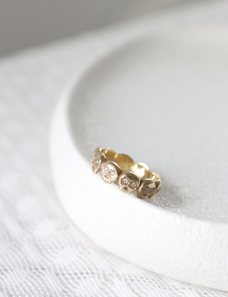May include: A gold ring with a band of small, detailed skull charms. Each skull has a small diamond for the eyes.