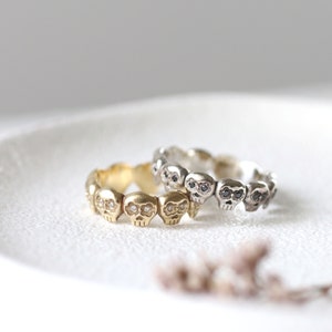 May include: Two skull rings with black and white diamonds. The ring on top is silver and the ring on the bottom is gold.