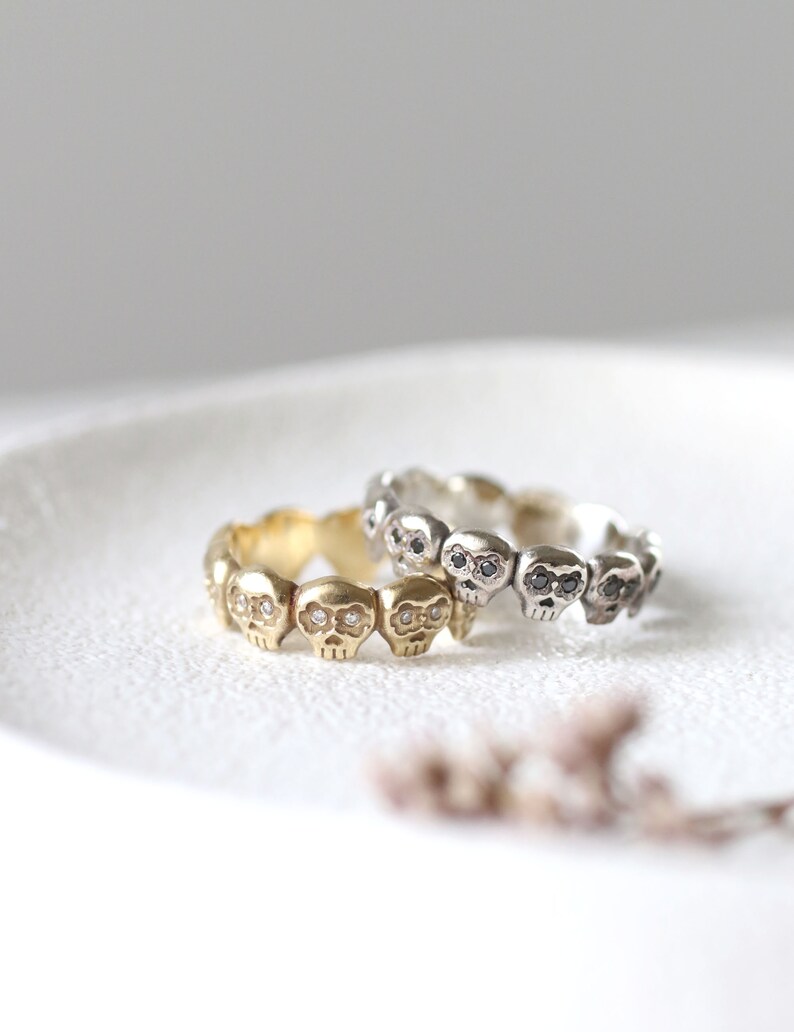 May include: Two skull rings with black and white diamonds. The ring on top is silver and the ring on the bottom is gold.