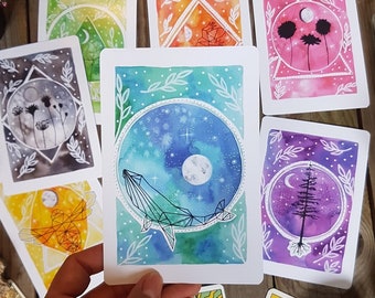 May include: Set of 8 watercolor cards featuring geometric shapes and nature-inspired designs. Each card has a different color background and a white outline of a whale, tree, or flower. The cards are perfect for adding a touch of whimsy to your home decor or for using as greeting cards.