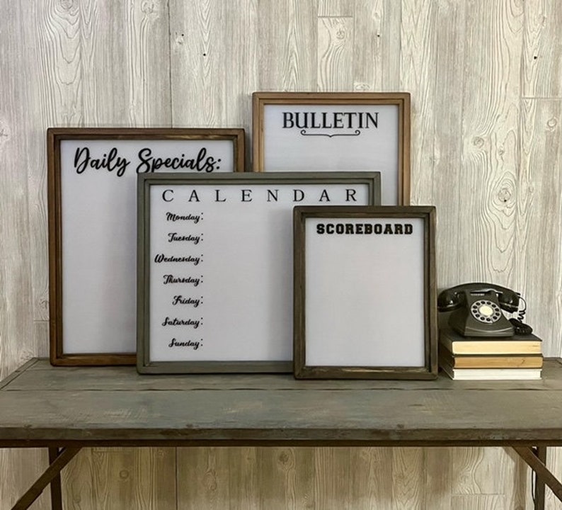 May include: Four framed whiteboards with black text. The top board says "BULLETIN" with a decorative flourish. The next board says "CALENDAR" and lists the days of the week. The third board says "SCOREBOARD". The bottom board says "Daily Specials:"
