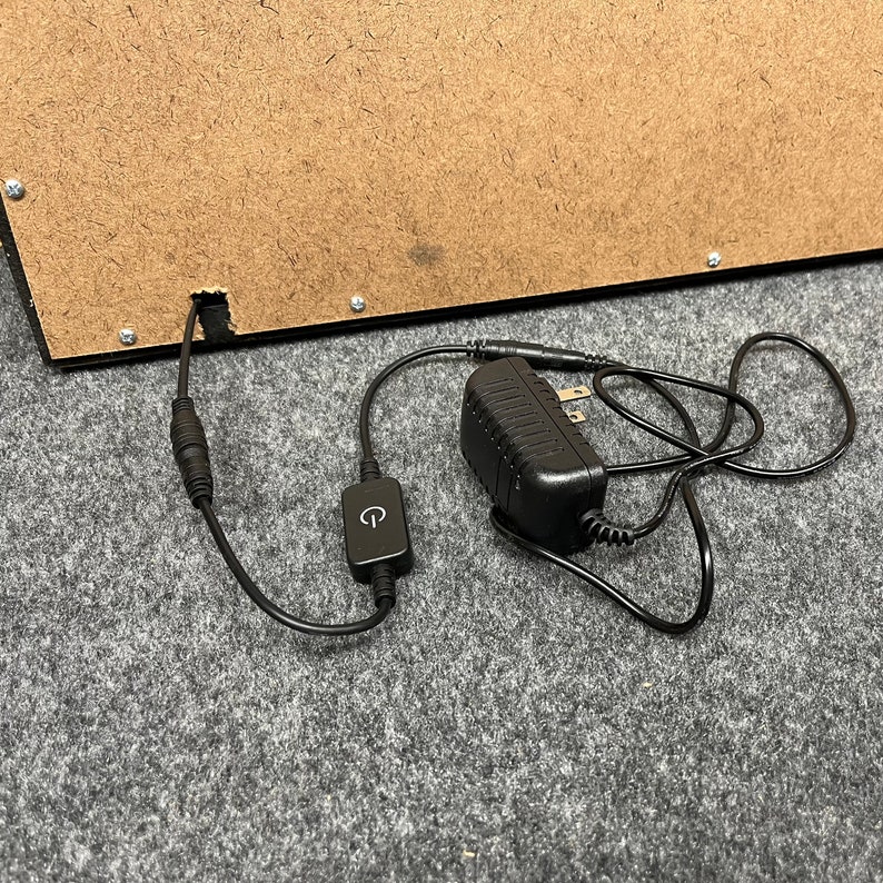 May include: Black power adapter with a black cord and a small black switch. The cord is plugged into a brown wooden box.