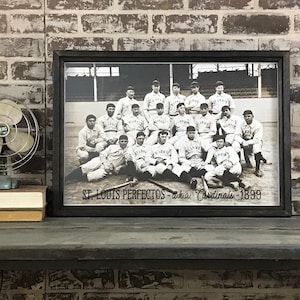 May include: Black and white photo of a baseball team, the St. Louis Perfectos, also known as the Cardinals, in 1899. The team is posed in front of a stadium, with their names and "St. Louis" written on their uniforms.