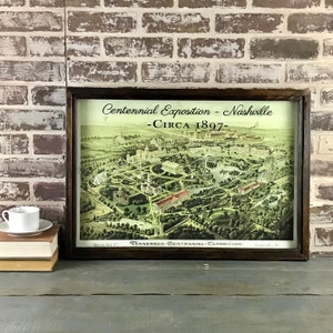 May include: A framed vintage map of the Tennessee Centennial Exposition in Nashville, circa 1897. The map is in a brown wooden frame and shows a detailed aerial view of the exposition grounds, including buildings, gardens, and walkways.