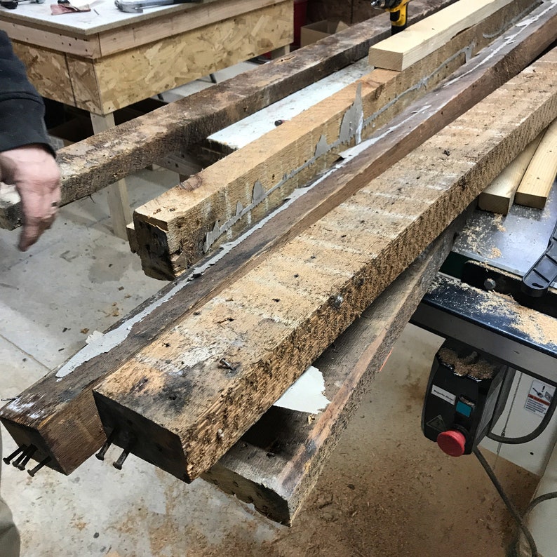 May include: Close-up of two weathered wooden beams joined together with glue. The beams are resting on a table saw with sawdust scattered around.
