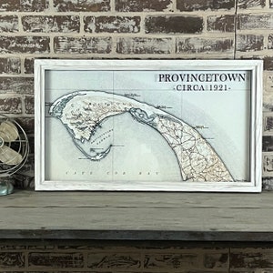 May include: A white framed map of Provincetown, Massachusetts, circa 1921. The map shows the coastline and surrounding area with detailed roads and landmarks. The title "Provincetown - Circa 1921 -" is printed in black at the top of the map.