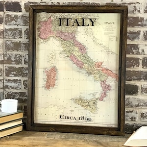 May include: A vintage map of Italy in a brown wooden frame. The map is printed on paper with a cream background and shows the regions of Italy in different colors. The map is titled "ITALY" and dated "CIRCA 1890".