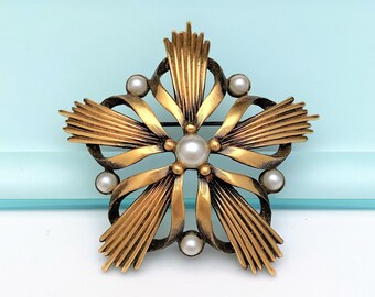 May include: A gold-toned brooch in the shape of a flower with a central pearl and smaller pearls around the edges.