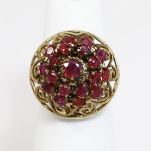 Puede incluir: Un anillo de oro con un racimo de rubíes rojos engastados en un delicado diseño de filigrana.