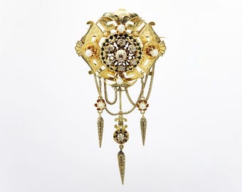 May include: A gold brooch with a central cluster of diamonds and pearls, surrounded by a decorative floral design. The brooch has three dangling chains with pearl and diamond accents.