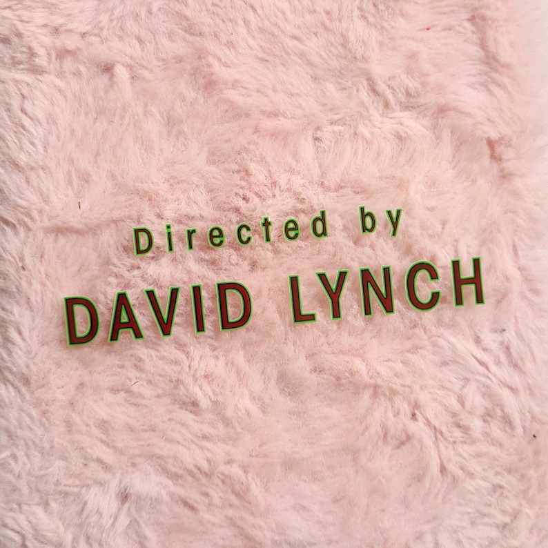 May include: A close-up of a pink, fluffy, textured surface. The text "Directed by DAVID LYNCH" is displayed in green and brown lettering. The image has a soft, inviting aesthetic.