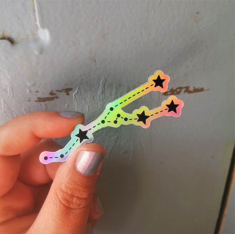 May include: A holographic sticker featuring a constellation of stars in a rainbow colour scheme. The sticker is shaped like the constellation Taurus, with five stars and a dotted line connecting them.