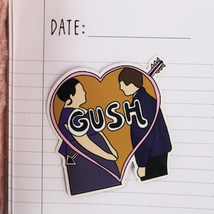 May include: A pink heart-shaped sticker with a cartoon couple inside. The couple is standing next to each other and the word "GUSH" is written in a stylized font in the middle of the heart.