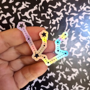 May include: A holographic sticker of the Aquarius constellation with black stars and a dashed line connecting them.