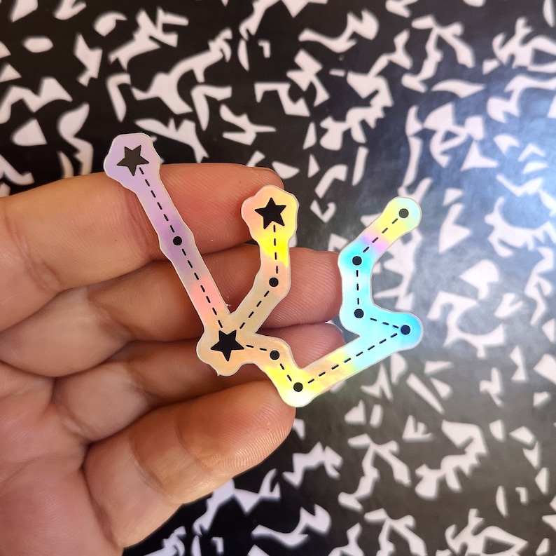 May include: A holographic sticker of the Aquarius constellation with black stars and a dashed line connecting them.