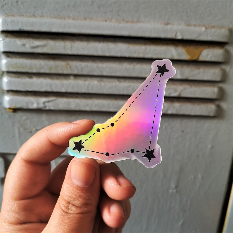 May include: A holographic sticker featuring a constellation of stars in a rainbow colour scheme. The sticker is shaped like a triangle and has a dotted line connecting the stars.