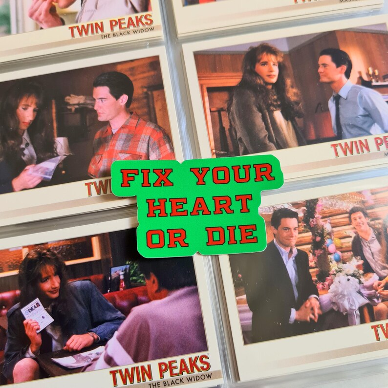 May include: A collection of Twin Peaks trading cards, featuring scenes from the show. A green sticker with the text "FIX YOUR HEART OR DIE" is placed over the cards. The cards are in protective sleeves.