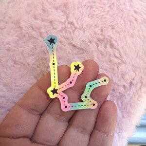 May include: A holographic sticker of the Aquarius constellation with black stars and a dashed line connecting the stars.