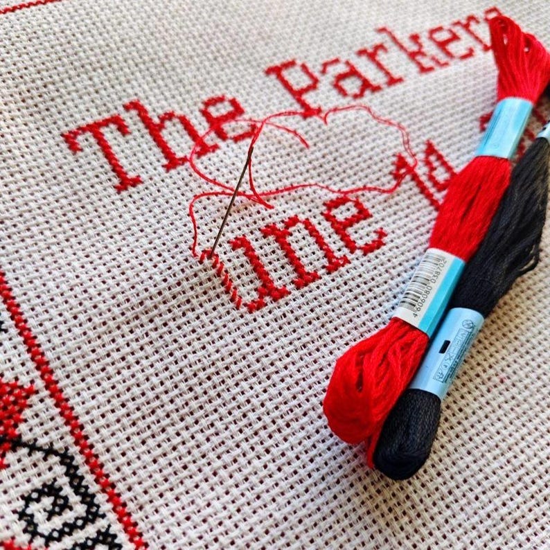 Behind-the-scenes shot of hand-embroidery in progress, showing needle and thread working on a part of the unique square red black personalized decorative pillow cover.