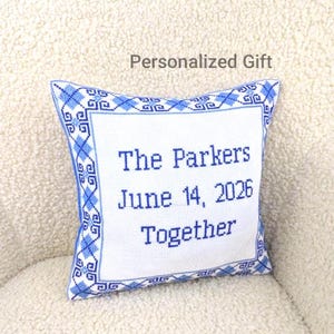 May include: A white square pillow with blue cross-stitch detailing and the words "The Parkers June 14, 2026 Together" in blue. The pillow has a blue patterned border and the text "Personalized Gift" above it.