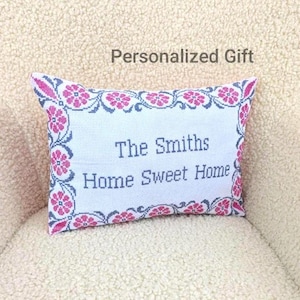 May include: A rectangular pillow with a white background and a floral border in pink and blue. The text "The Smiths Home Sweet Home" is embroidered on the pillow. The words "Personalized Gift" are above the pillow.