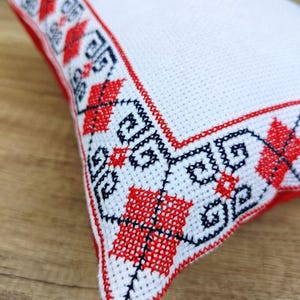 Close-up detail of high-quality hand-stitched custom embroidery of square red black personalized decorative pillow cover, showing fine needlework texture on  fabric.