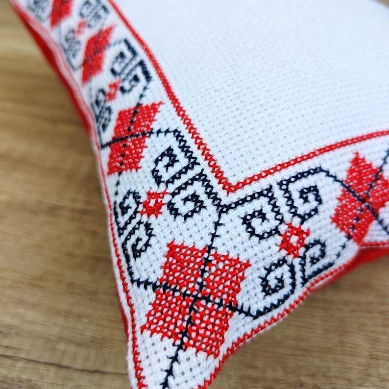 Close-up detail of high-quality hand-stitched custom embroidery of square red black personalized decorative pillow cover, showing fine needlework texture on  fabric.