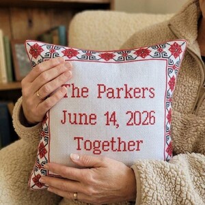 Square red black personalized decorative pillow  held in hands to demonstrate size, scale, and the premium texture of the embroidered fabric.