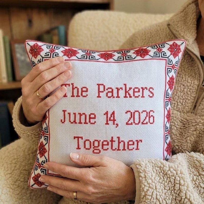 Square red black personalized decorative pillow  held in hands to demonstrate size, scale, and the premium texture of the embroidered fabric.