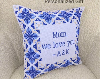 May include: Square white pillow with blue and tan geometric embroidery. The pillow has the text "Mom, we love you - A&K" in blue. The pillow is a personalized gift.
