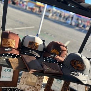 Peut inclure: Un présentoir de casquettes de camionneur marron, blanc et gris avec des motifs brodés. Les casquettes sont disposées sur une étagère avec des cadres photo en cuir et d'autres articles en cuir.