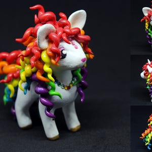 May include: A white unicorn figurine with a rainbow mane and tail. The mane is a vibrant mix of red, orange, yellow, green, blue, and purple, with matching tail. The unicorn has a beaded necklace and gold hooves. The background is black.