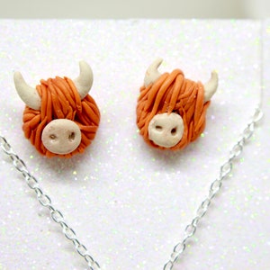 May include: A pair of orange and white Highland cow earrings with a silver chain necklace.