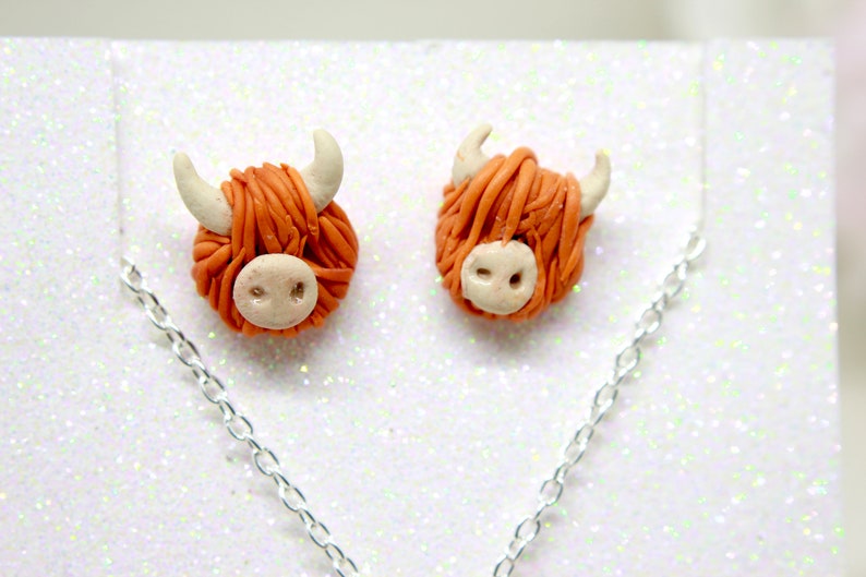 May include: A pair of orange and white Highland cow earrings with a silver chain necklace.