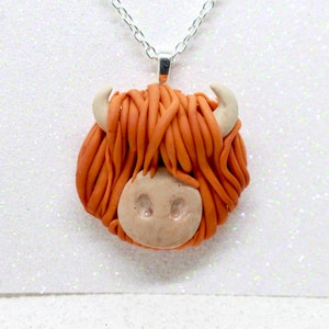May include: A necklace with a handmade orange and brown clay pendant shaped like a Highland cow head.