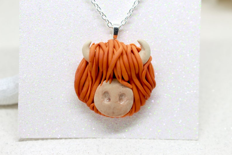 May include: A necklace with a handmade orange and brown clay pendant shaped like a Highland cow head.