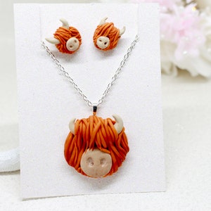 May include: A set of Highland Cow earrings and a necklace. The earrings and pendant are made of orange and white polymer clay and feature a Highland Cow head with fluffy hair.