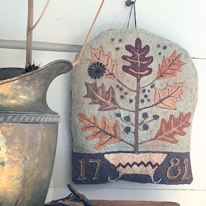 Puede incluir: Un tapiz de pared de punto de aguja hecho a mano que presenta un árbol estilizado con hojas marrones y naranjas, bayas azules y una maceta marrón. Las fechas 1781 están cosidas en la parte inferior de la pieza.