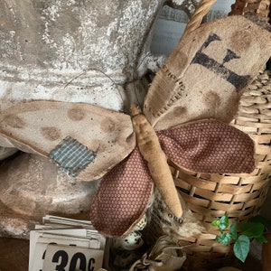 Peut inclure: Un papillon en tissu fait main avec des tissus patchwork marron, blanc et bleu. Le papillon est fixé à un bâton en bois et a un tissu à motifs marron, blanc et rouge sur les ailes.