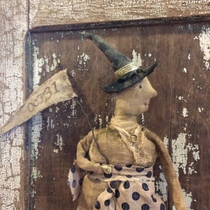 May include: A handmade rag doll witch wearing a black hat and a polka dot skirt. The doll is holding a banner that says "Oct 31".