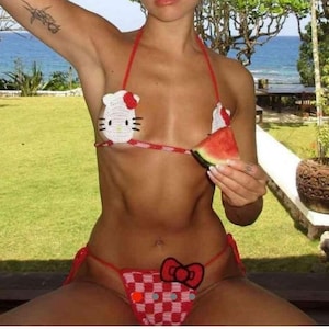 May include: A red and white crochet bikini set featuring a Hello Kitty design on the top and a checkered pattern on the bottom. The bikini is made of a soft, lightweight material, perfect for a day at the beach or pool.