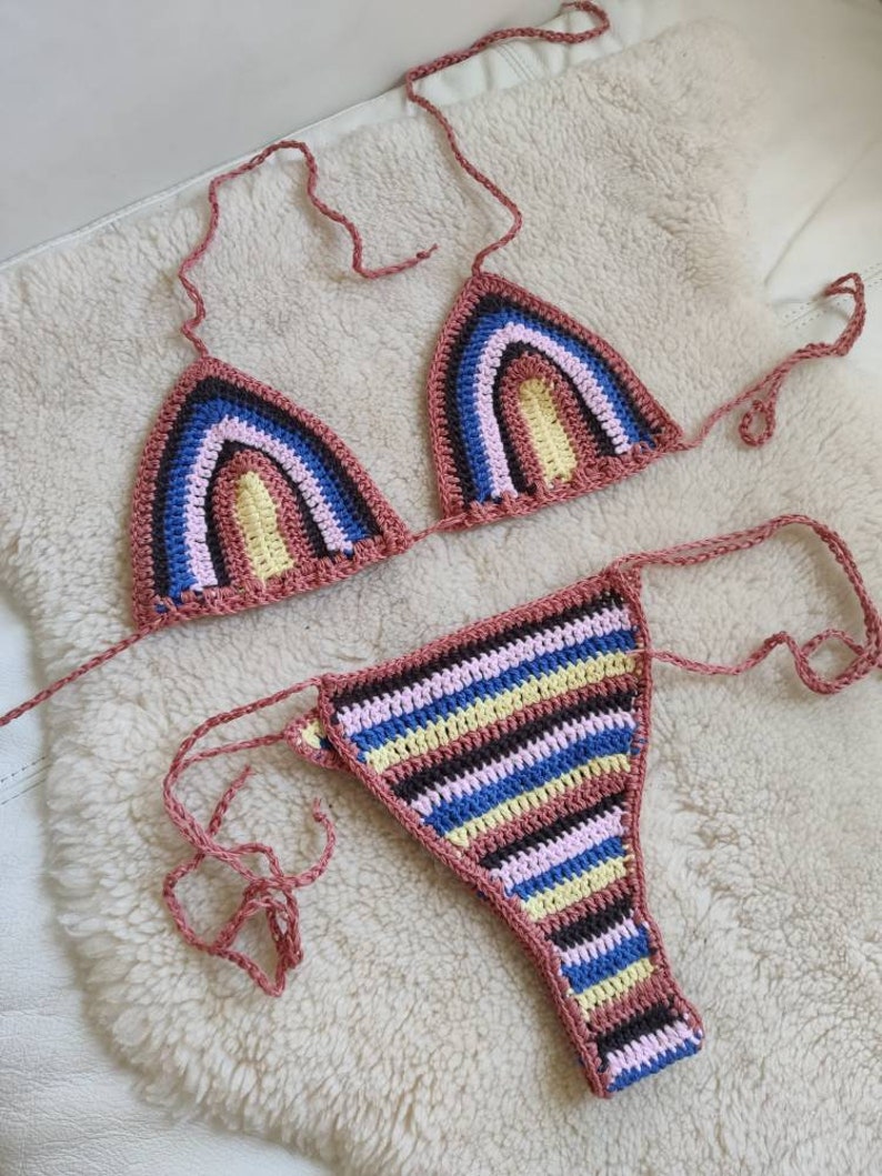 May include: A crocheted bikini top and bottom with a rainbow stripe pattern in pink, yellow, blue, brown, and black. The bikini is made with a thick yarn and has a simple design.