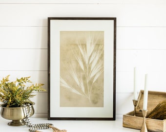 May include: A white dresser with a framed botanical print of a dried plant, a gold planter with a green plant, a wooden box with dried grasses, and two candlesticks with white candles.