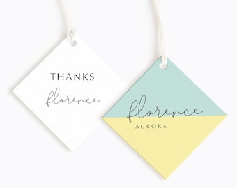 Könnte beinhalten: Zwei diamantförmige Geschenkanhänger mit weißem Hintergrund und schwarzem Text. Der erste Anhänger lautet "THANKS florence". Der zweite Anhänger ist diagonal geteilt mit einem hellblauen oberen Teil und einem gelben unteren Teil. Der Text auf dem zweiten Anhänger lautet "florence AURORA".