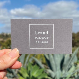 May include: A gray business card with a white border around the text "brand name or logo".