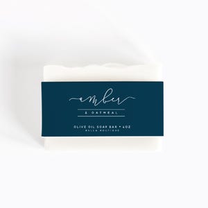 May include: A white bar of soap with a navy blue label that reads "amber & oatmeal" and "Olive Oil Soap Bar - 4 oz. Bella Boutique".