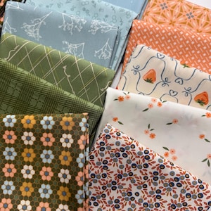 May include: A collection of folded fabric squares featuring diverse patterns including blue floral prints, green plaid, orange geometric designs, white strawberry motifs, small orange flowers, and a dark green background with repeating flower shapes.