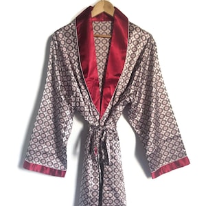 May include: A long-sleeved robe with a burgundy trim and a white background with a repeating pattern of small circles. The robe has a tie belt and is made of a silky material.