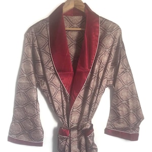 May include: A long-sleeved robe with a paisley pattern in shades of brown and cream. The robe has a burgundy satin collar and trim. The robe has a tie belt.